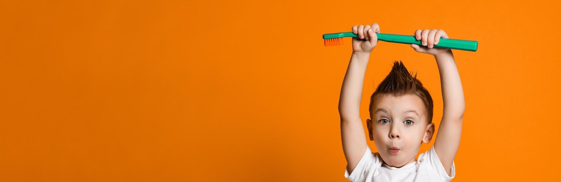 Little boy holding up enlarged tooth brush against orange background